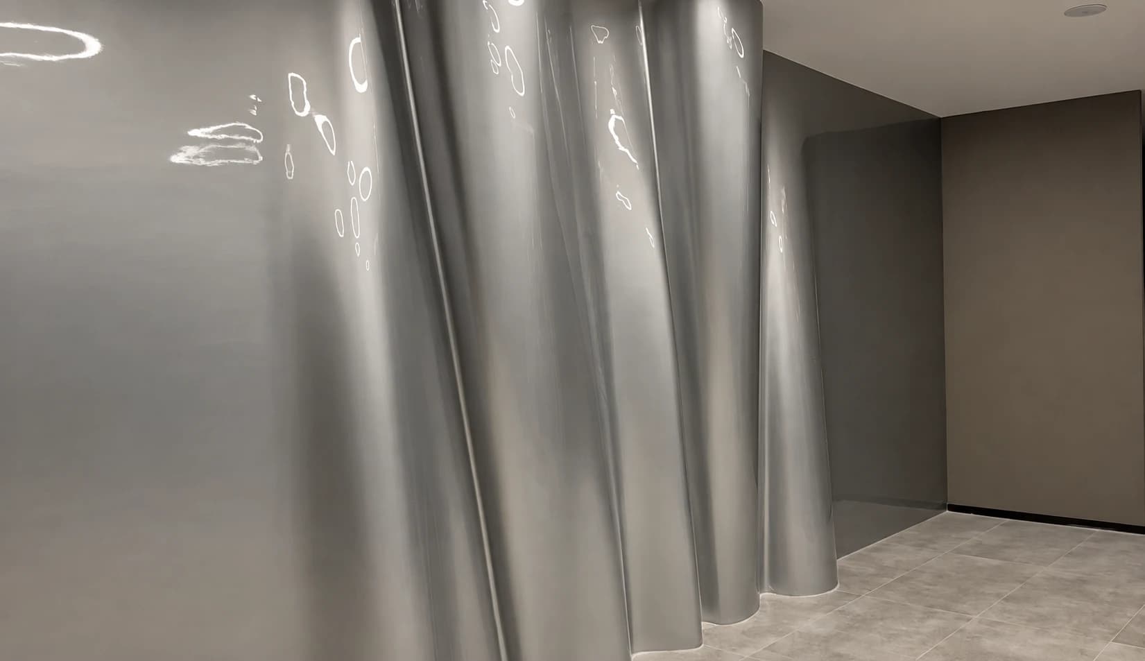 Close view of curved silver-grey wall panels and surface reflections